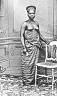  
Code: 0002 4046
Category: People from Elmina

Three portraits of Elmina women, unidentified
1. Young lady with bare breasts, possibly an engagement picture.

This set of three portraits is not identified by Muller. Possibly he regarded the portraits of women in traditional dress as ethnographic curiosities. The compositions of the portraits indicates, however, that these are photo's made for the use of the depicted persons themselves.
The young woman shows her virginity by showing her bared breasts. A portrait like this was often made in well to-do circles to commemorate the engagement of the girl in question. The group portrait of two women and two girls seems to be a family group of three generations (grandmother, mother, daughters).
