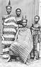  
Code: 0002 4048
Category: People from Elmina

Three portraits of Elmina women, unidentified
3. Possibly a family group of three generations of women, formal portrait.

This set of three portraits is not identified by Muller. Possibly he regarded the portraits of women in traditional dress as ethnografic curiosities. The compositions of the portraits indicates, however, that these are photo's made for the use of the depicted persons themselves.
The young woman shows her virginity by showing her bared breasts. A portrait like this was often made in well to-do circles to commemorate the engagement of the girl in question. The group portrait of two women and two girls seems to be a family group of three generations (grandmother, mother, daughters).


